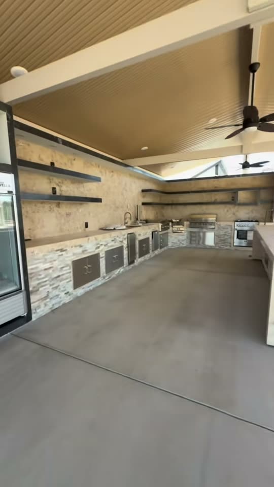Unstaged daytime view of a stone U-shaped outdoor kitchen with stainless doors and bare shelves