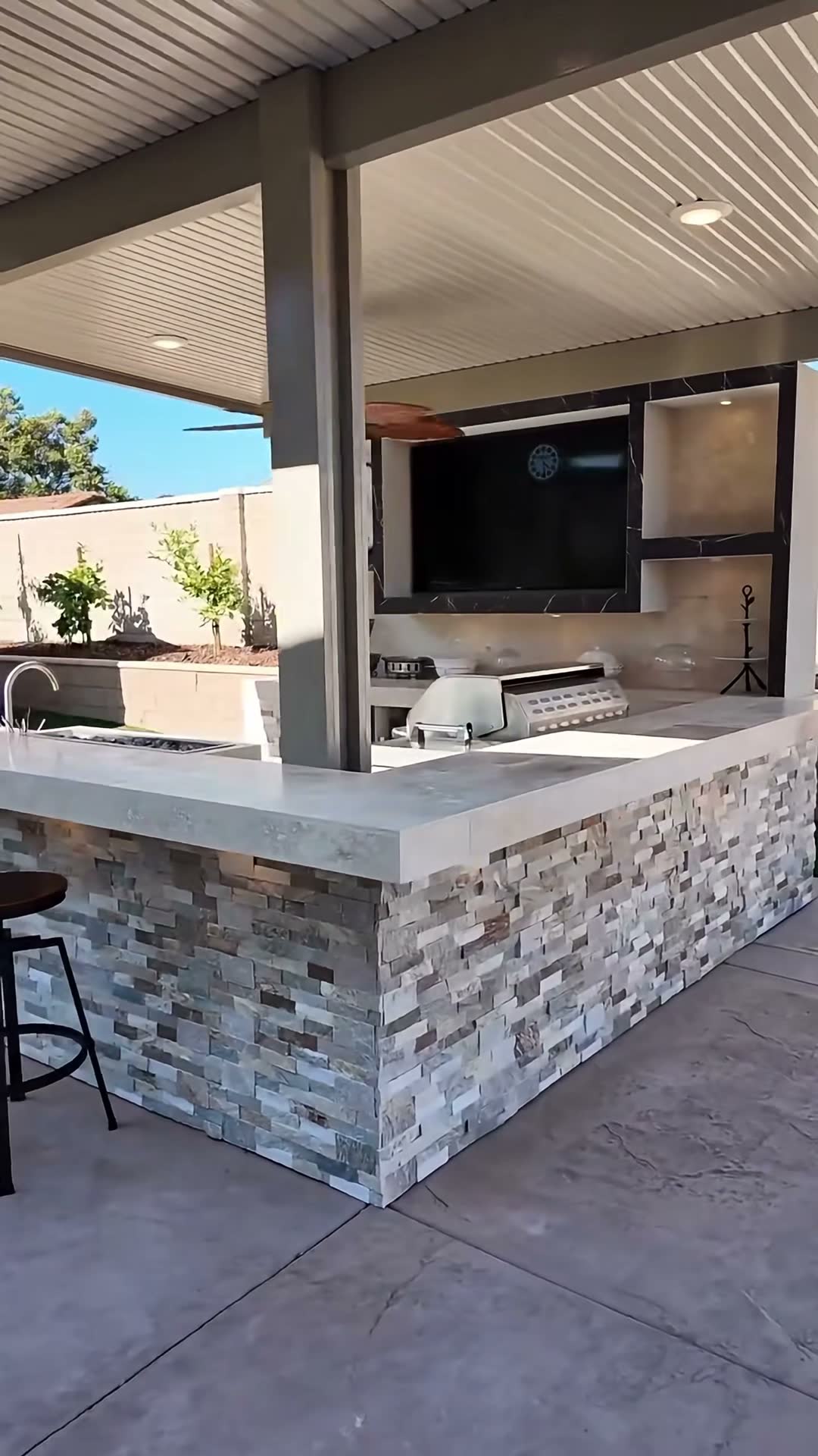 L-shaped stacked-stone kitchen bar with sink, side burner and griddle beneath an alumawood patio cover
