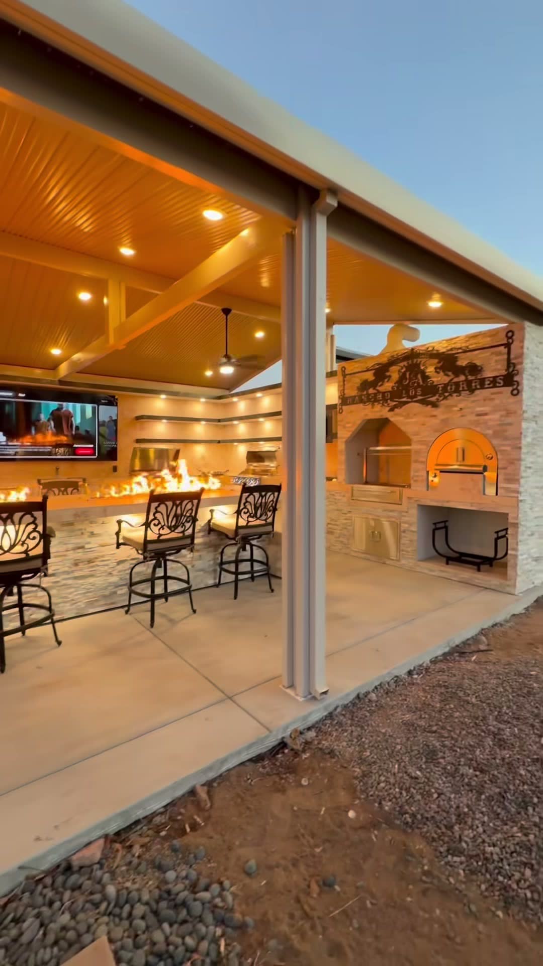 Gable patio cover over a fire-trough bar, with a stone pizza oven and wood-burning fireplace alongside