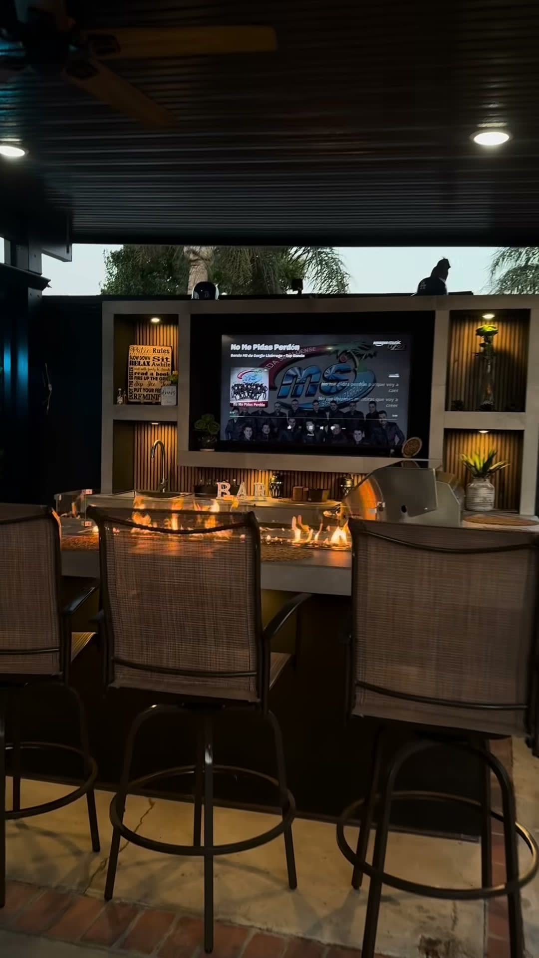 Fire trough burning the length of a bar beneath a TV wall with lit niches at dusk
