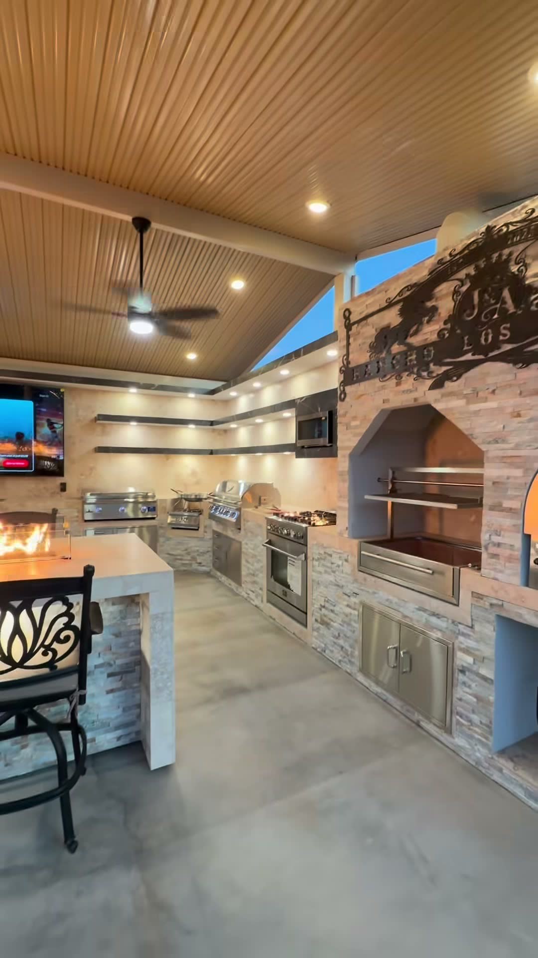 Stone U-shaped outdoor kitchen with grill, gas range, santa maria grill and wood-fired pizza oven