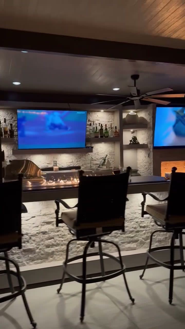 Close view of a white stone bar with fire glass burner, stainless grill and two mounted TVs at night