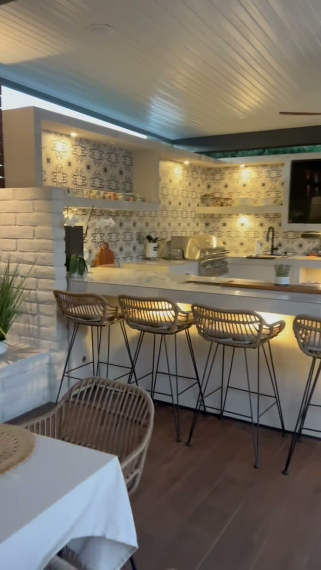 White bar counter with rattan stools and a patterned tile kitchen behind, under a plank patio cover