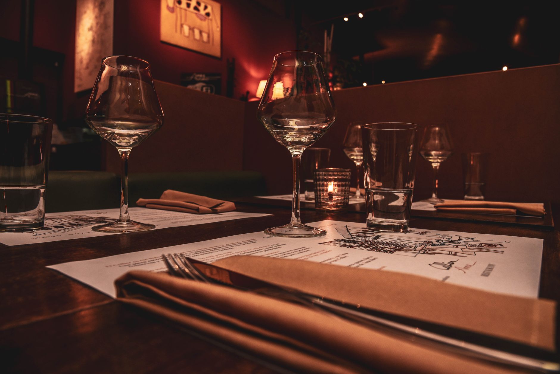 A candlelit dinner table set with wine glasses and a printed menu