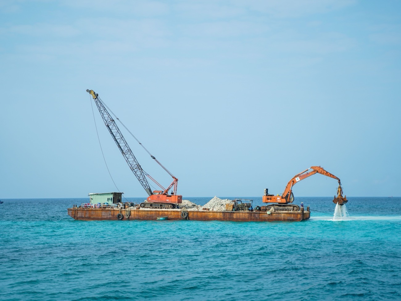 A barge carrying two excavators, working on open water