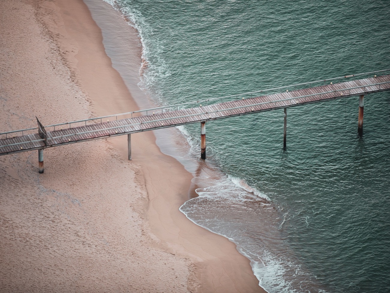 Aerial view along a timber pier running out from a beach into open water