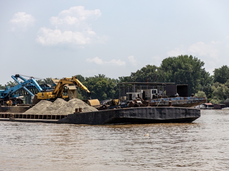 A barge carrying excavators and a load of sand, working off a shoreline