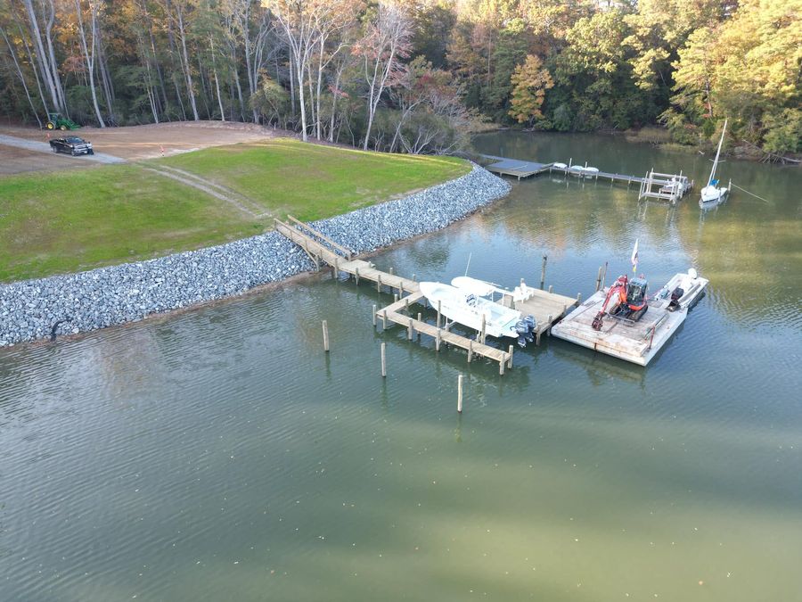 Aerial view of a timber walkway crossing a new granite riprap revetment onto a dock with a boat lift, the work barge tied alongside