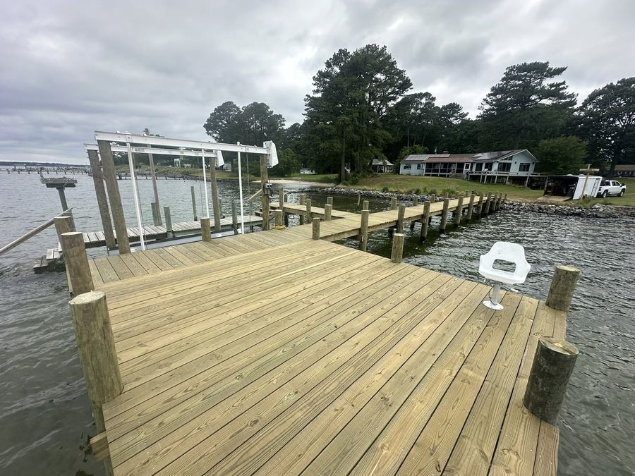 A four-post aluminium boat lift standing on a newly built timber dock, waterfront houses across the creek