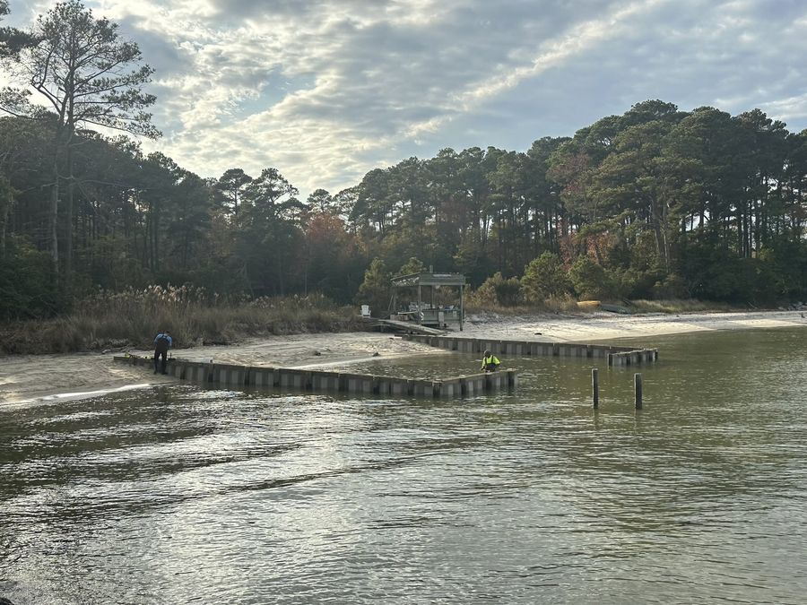 Crew driving a line of sheet piles across a shallow creek mouth at low water