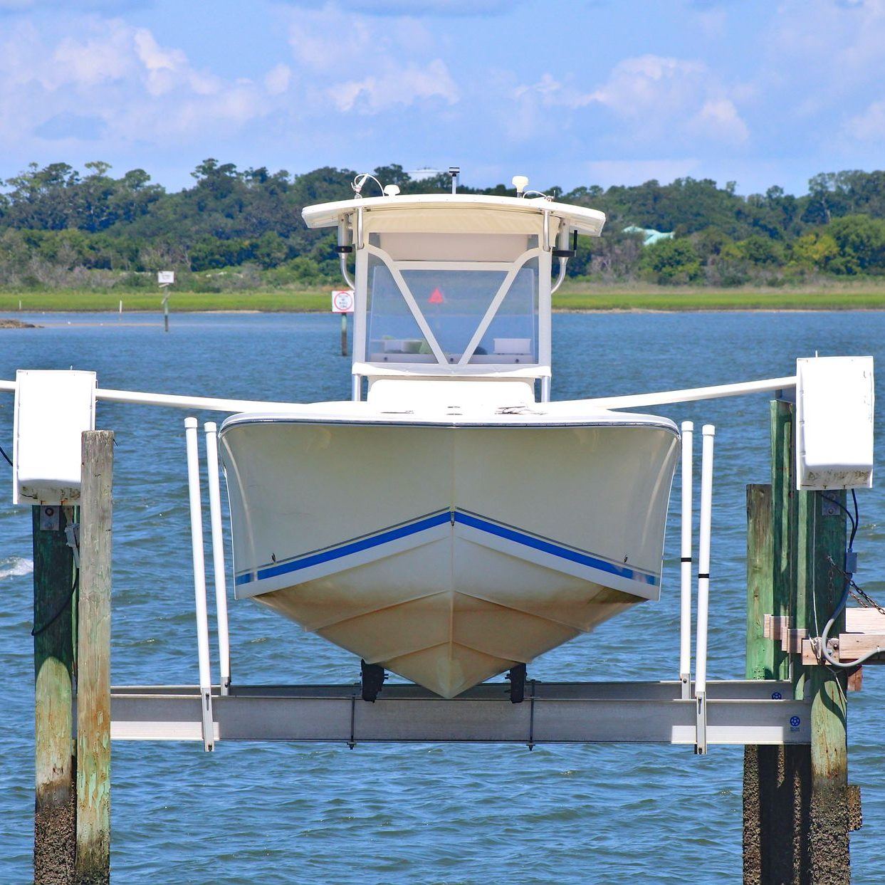 White center-console boat raised out of the water on an aluminum boat lift beside dock pilings