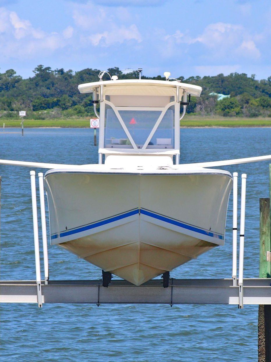 White center-console boat raised out of the water on an aluminum boat lift beside dock pilings