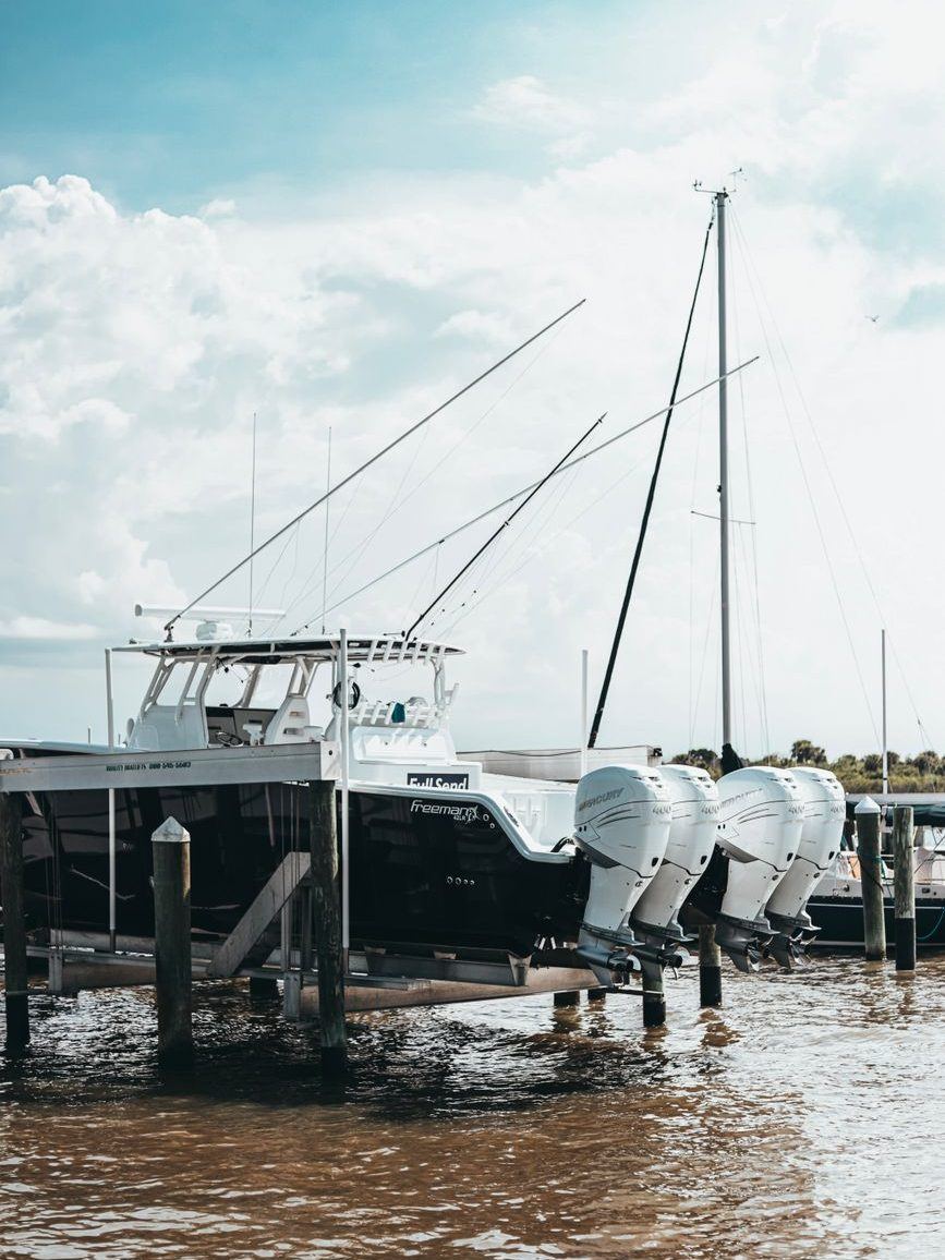 Sport-fishing boat with twin outboards tied at a timber dock in shallow water