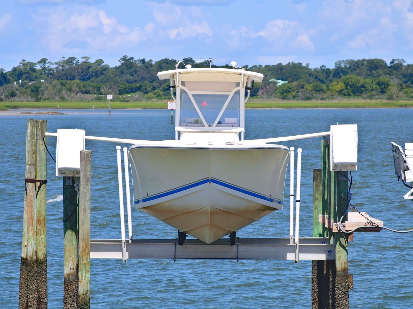 White center-console boat raised out of the water on an aluminum boat lift beside dock pilings