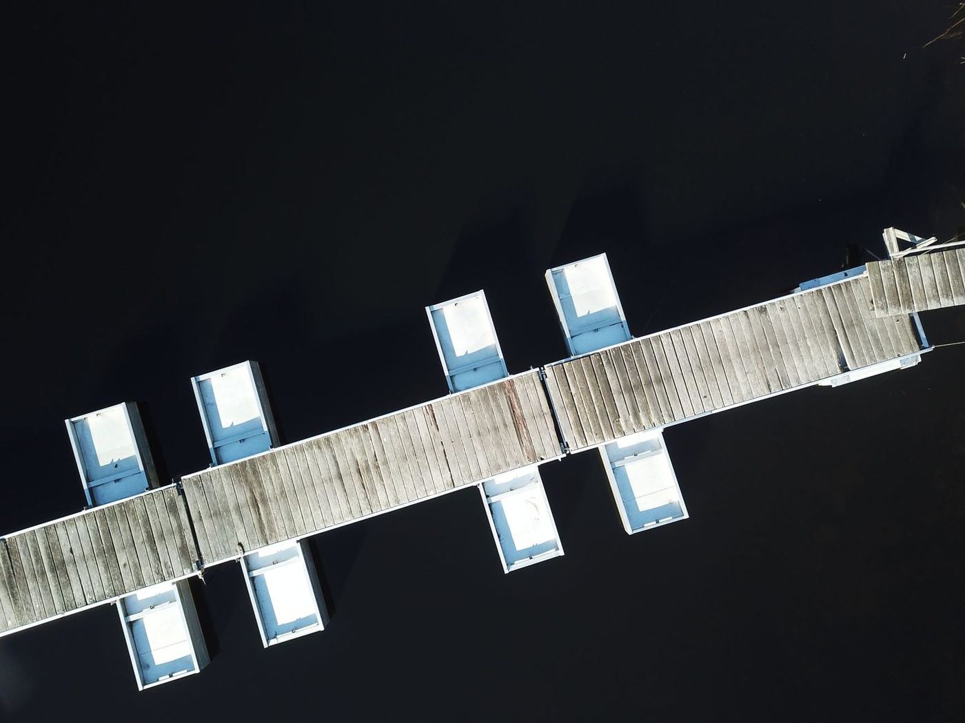 Aerial view of a floating dock system with gangway and empty berths on dark water