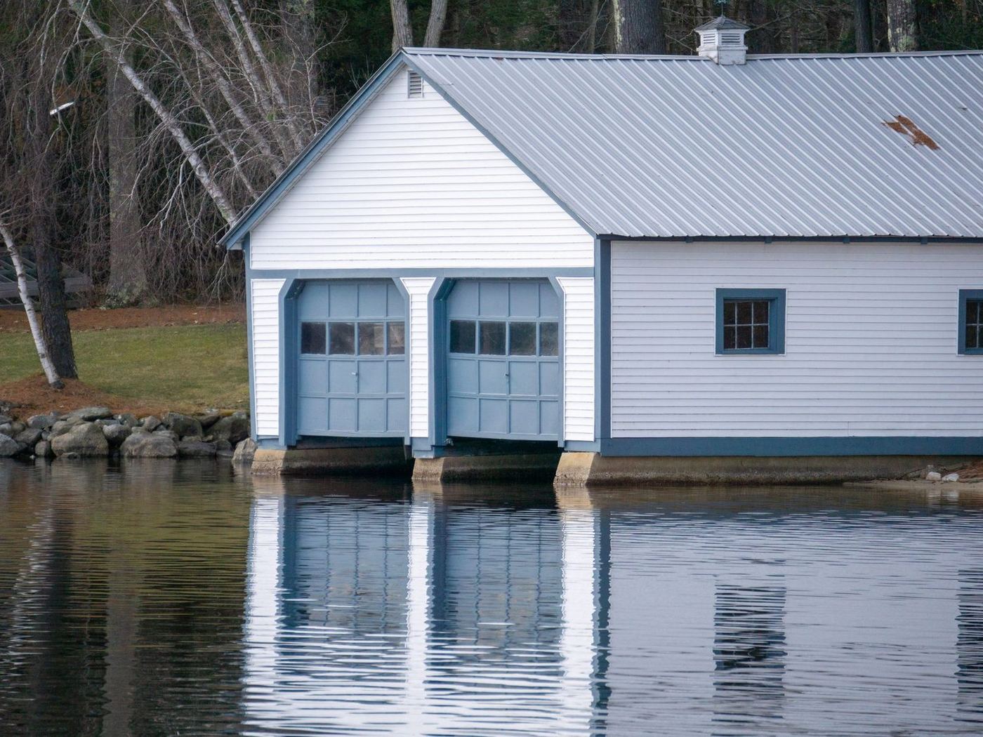 White boathouse with a metal roof and double doors built out over a lake
