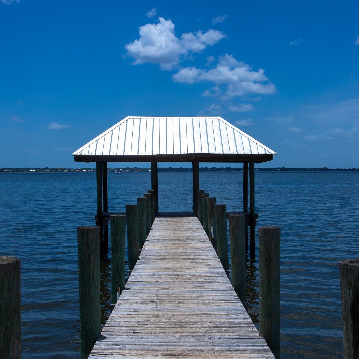 Covered dock with a white metal roof at the end of a timber pier over open water