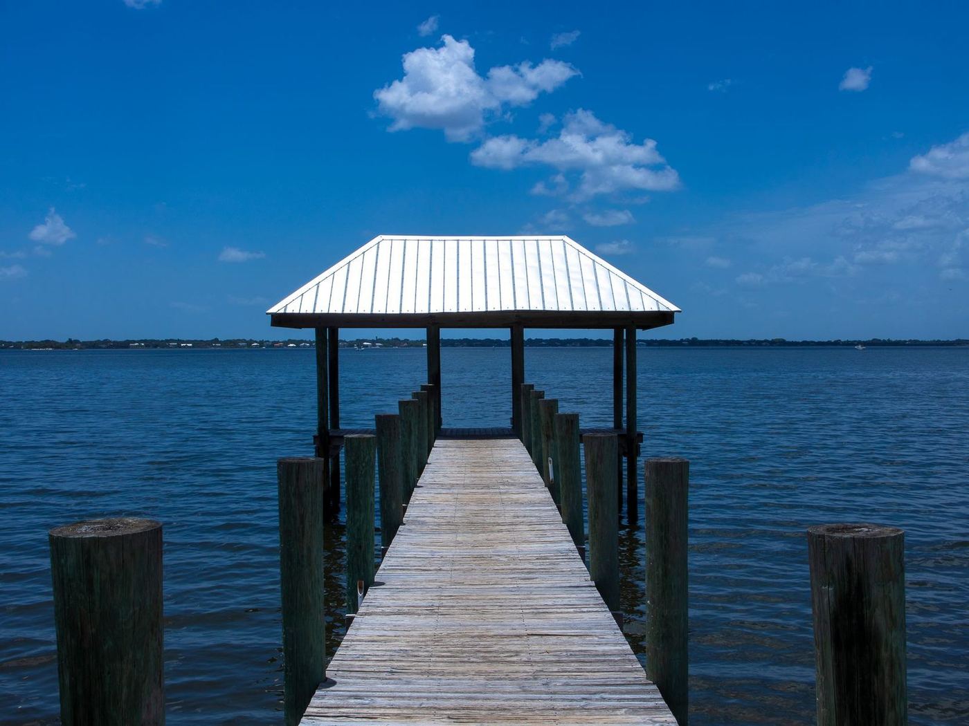 Covered dock with a white metal roof at the end of a timber pier over open water