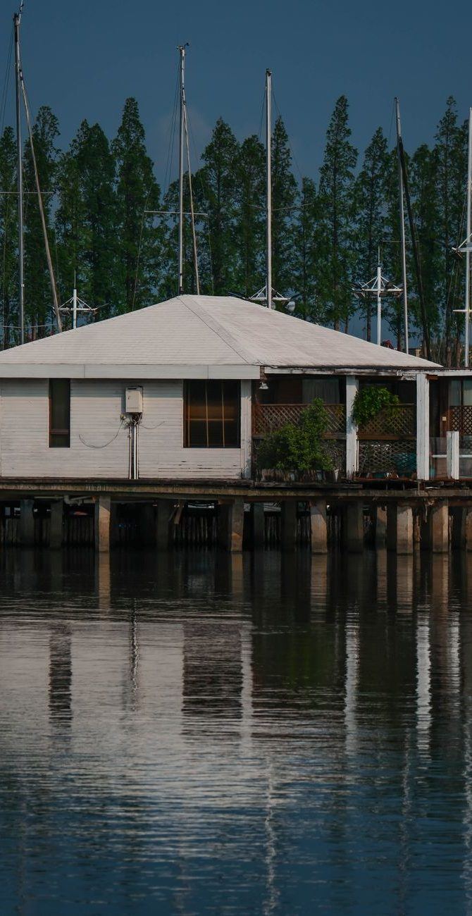 Boathouse standing on tall pilings over the water with masts behind it