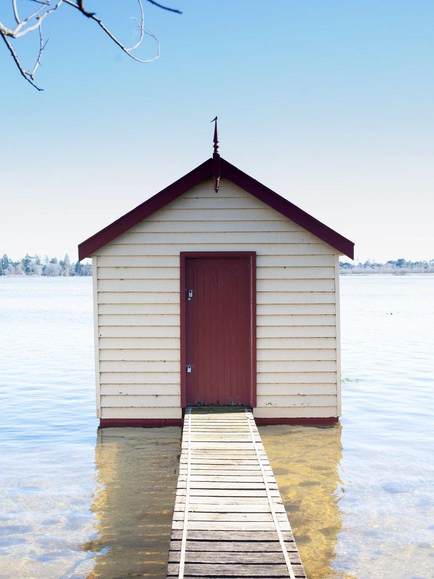 White boat shed at the water's edge with a slipway running down into the shallows