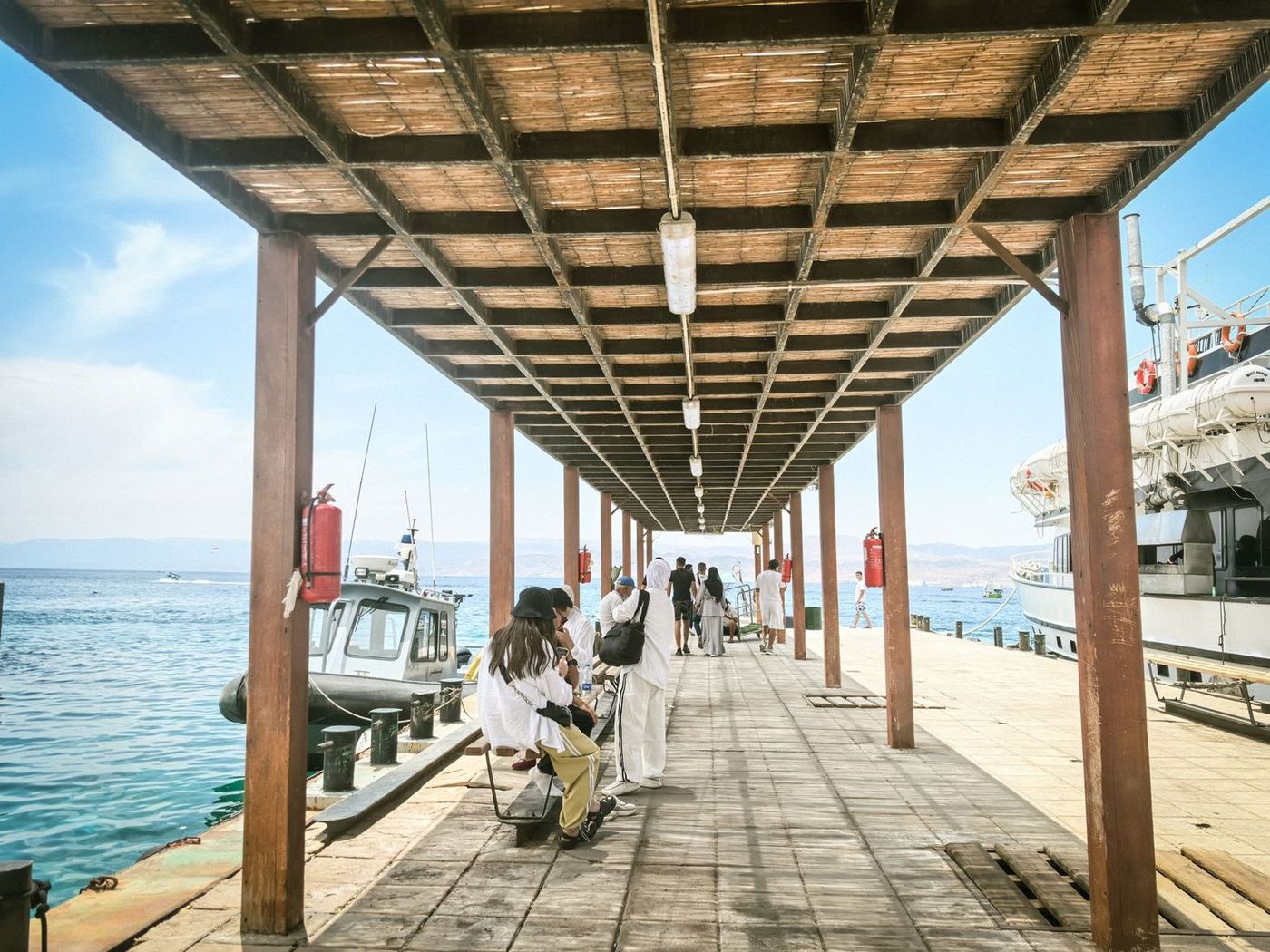 Looking down a covered pier walkway under timber rafters, open water beyond the posts