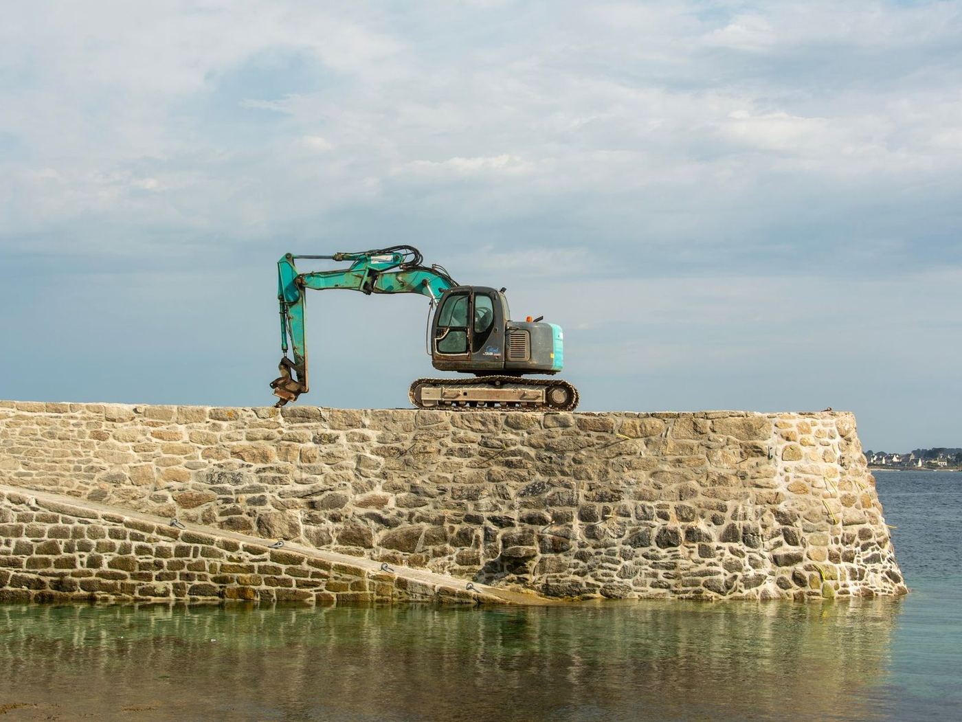 Excavator working on top of a stone sea wall out over the water