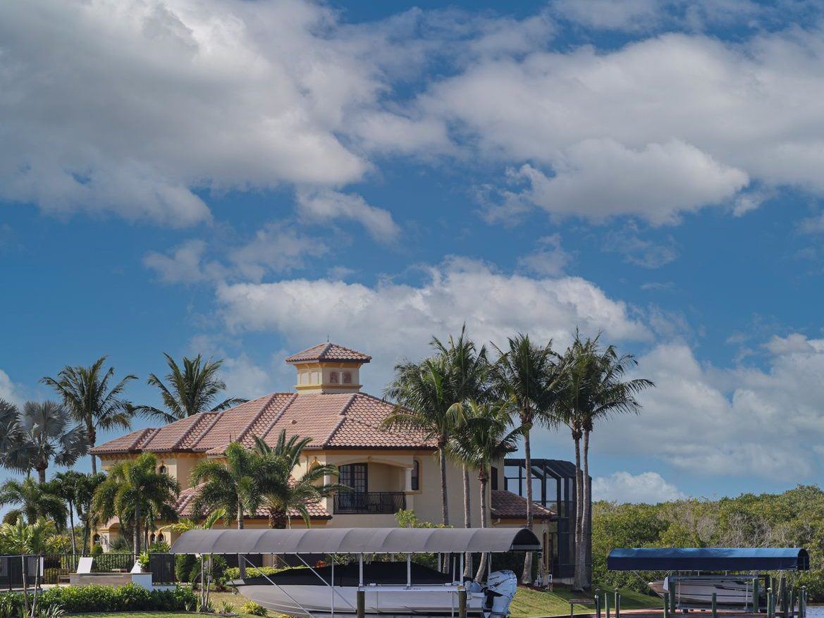 Waterfront boathouse with a tiled roof and open deck beside palm trees and a dock