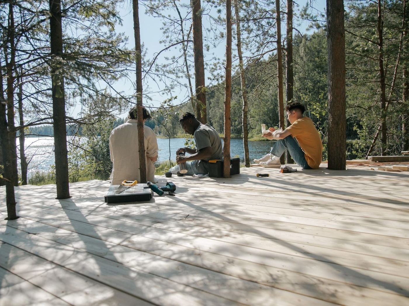 Crew working together on a new timber deck among tall pines beside a lake