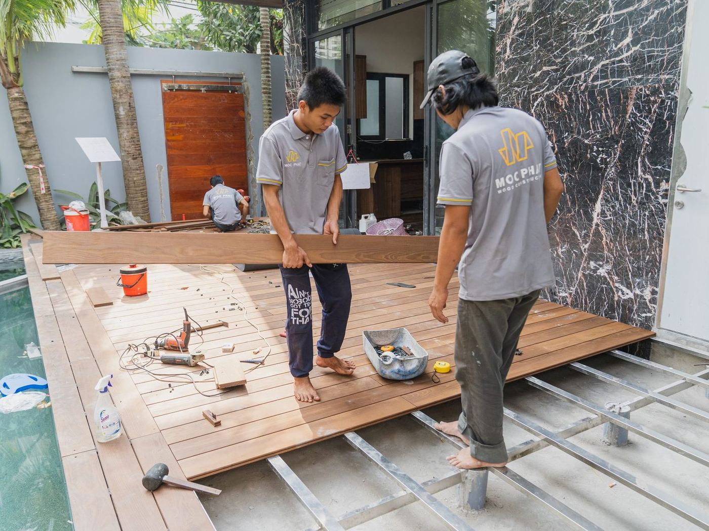 Two workers laying timber decking boards over a steel frame beside a pool