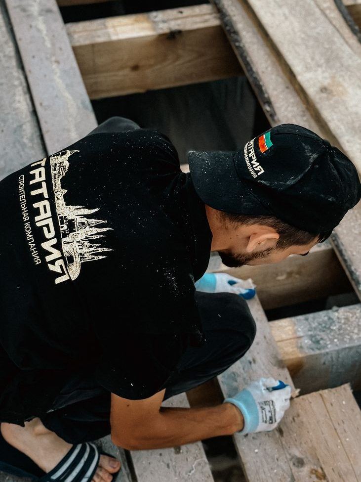 Worker crouched on a timber deck fixing a replacement board into place