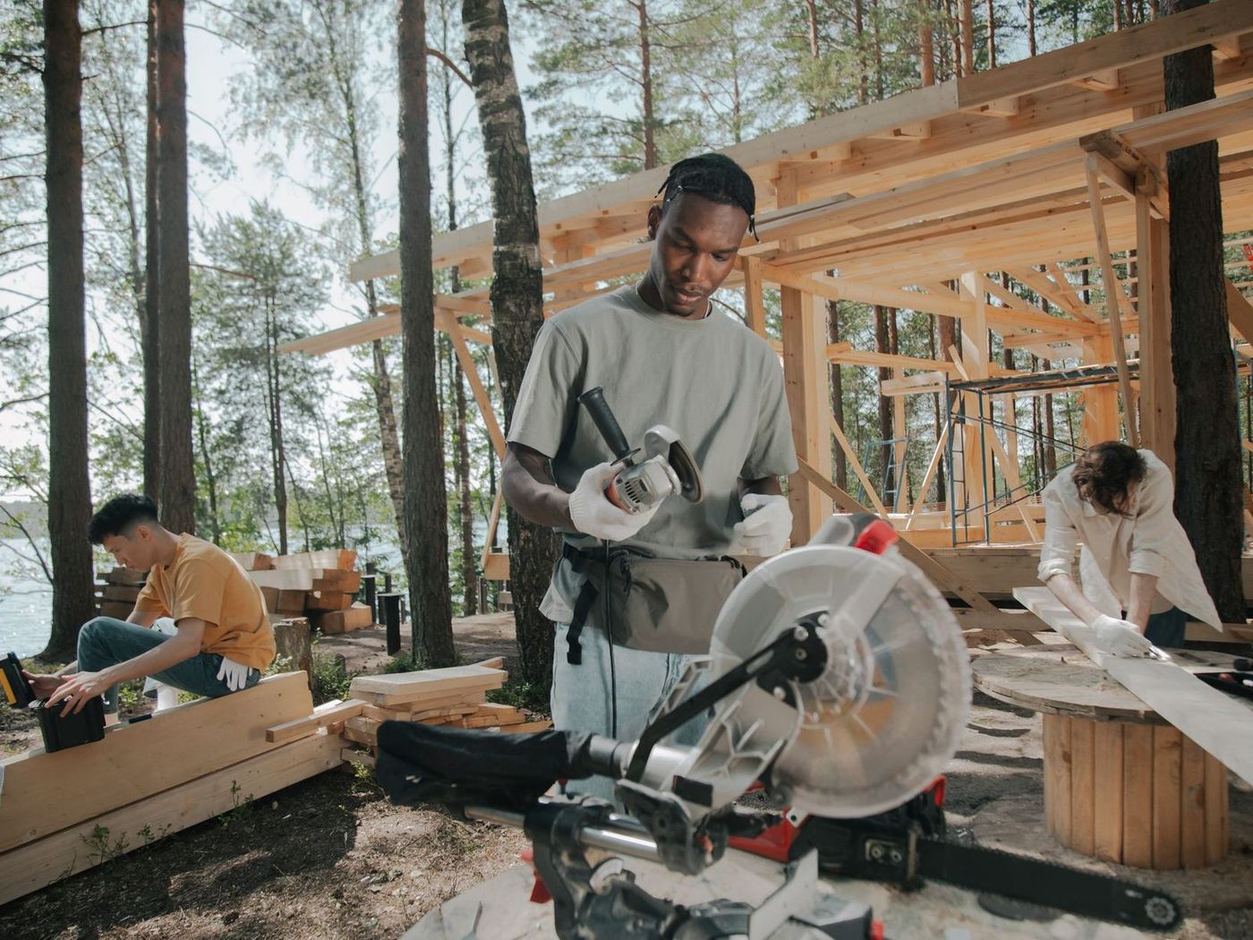 Carpenter cutting timber on a mitre saw at a lakeside frame build, crew working behind