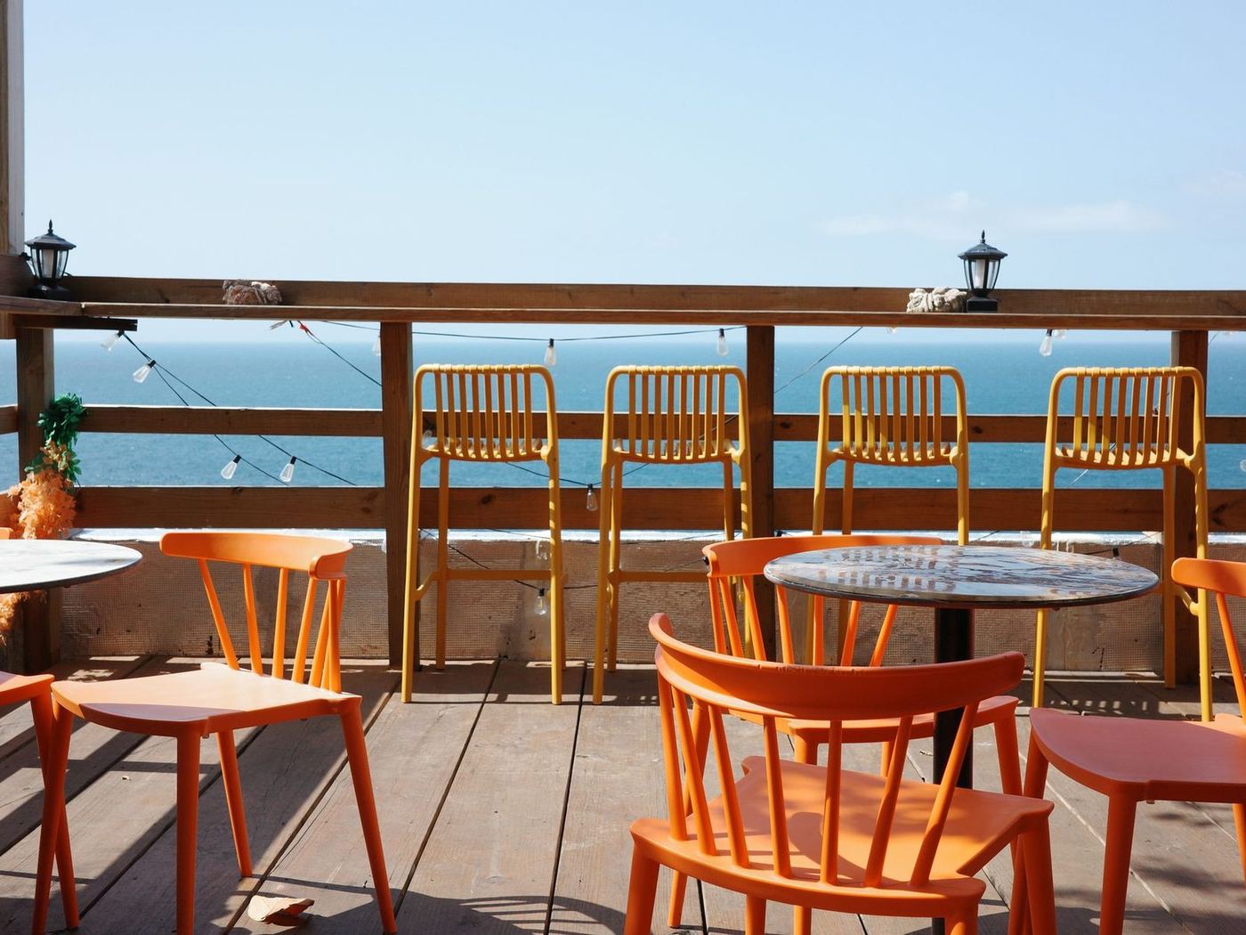 Timber deck with chairs and tables along a railing looking straight out to sea