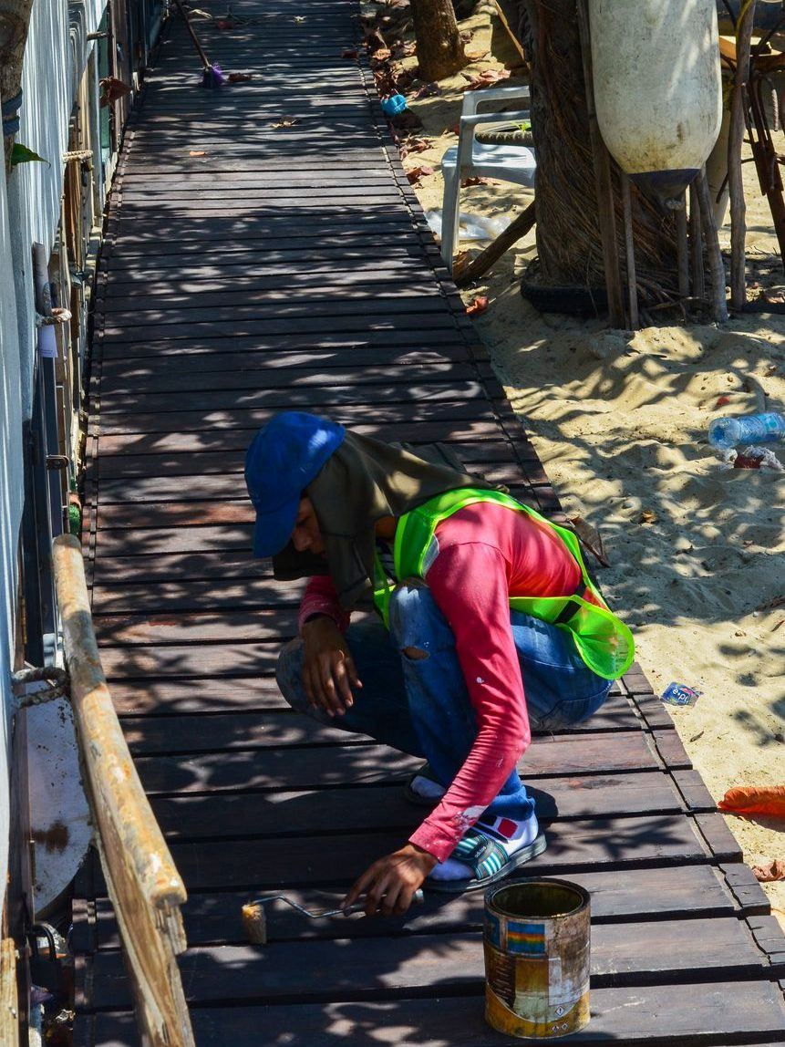 Worker on their knees staining the boards of a long timber walkway