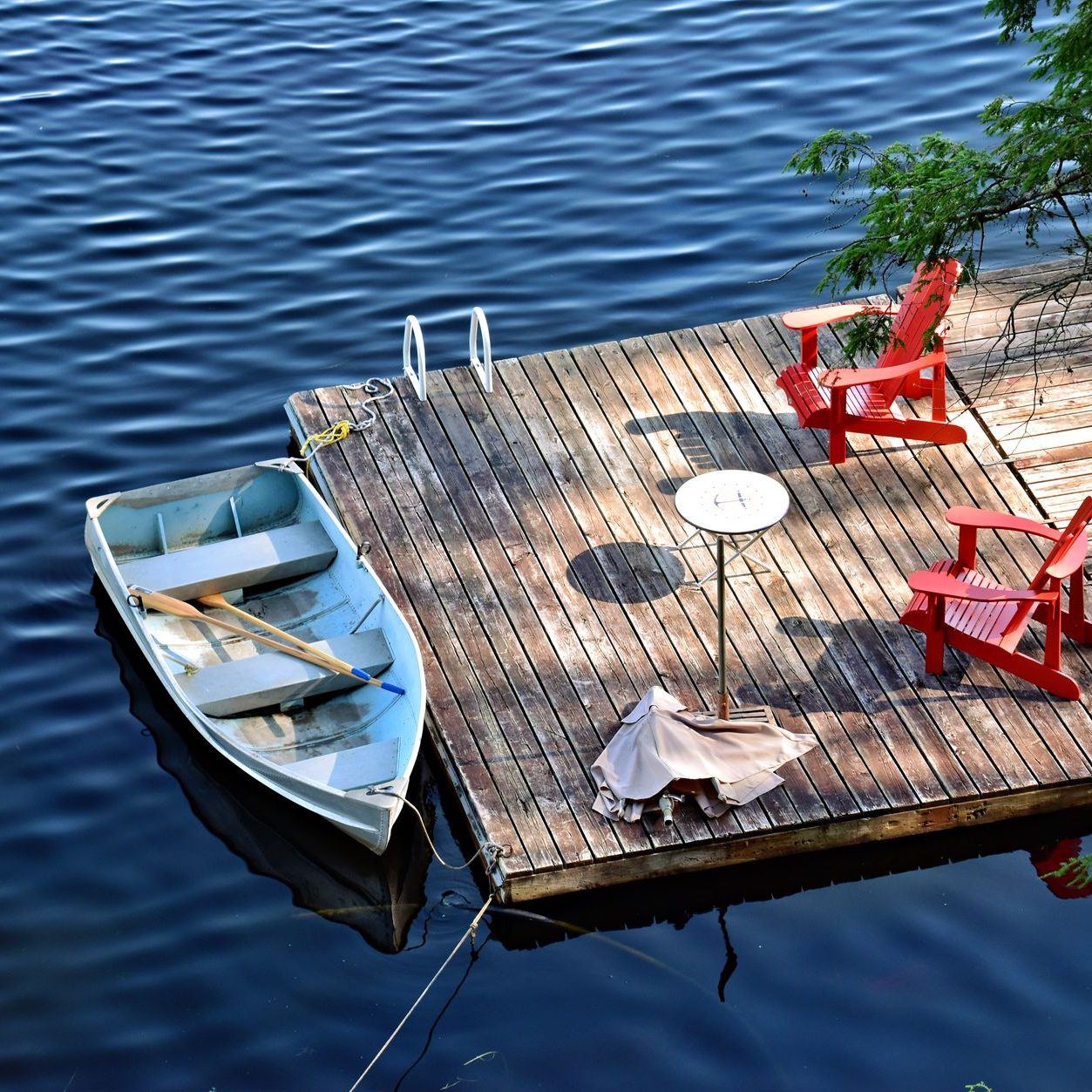 Timber dock with chairs and a table set out on it, a rowboat tied alongside