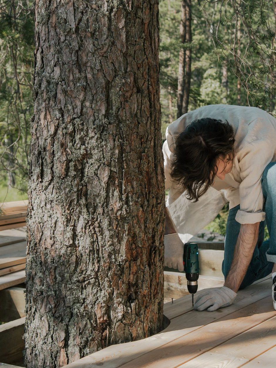 Worker kneeling on new decking to fix a board down beside a tree