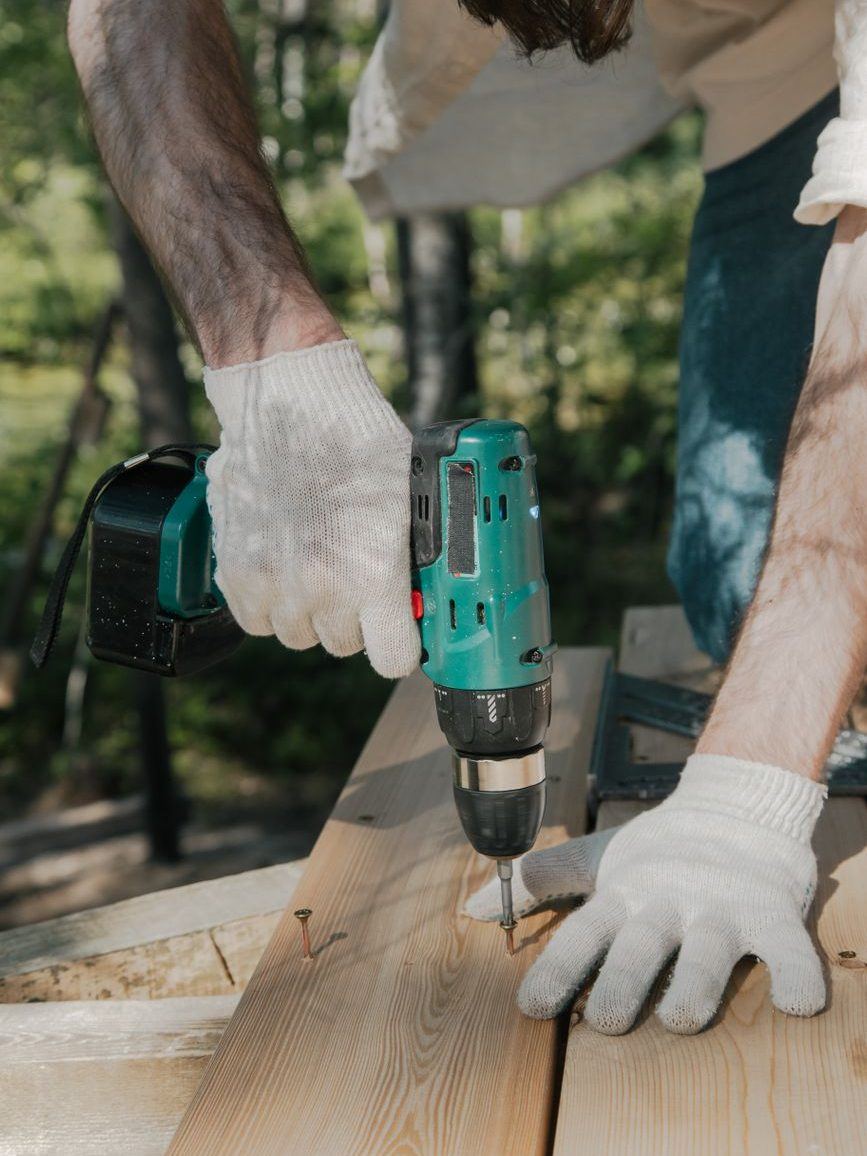 Gloved hands driving a screw into a new decking board with a cordless drill