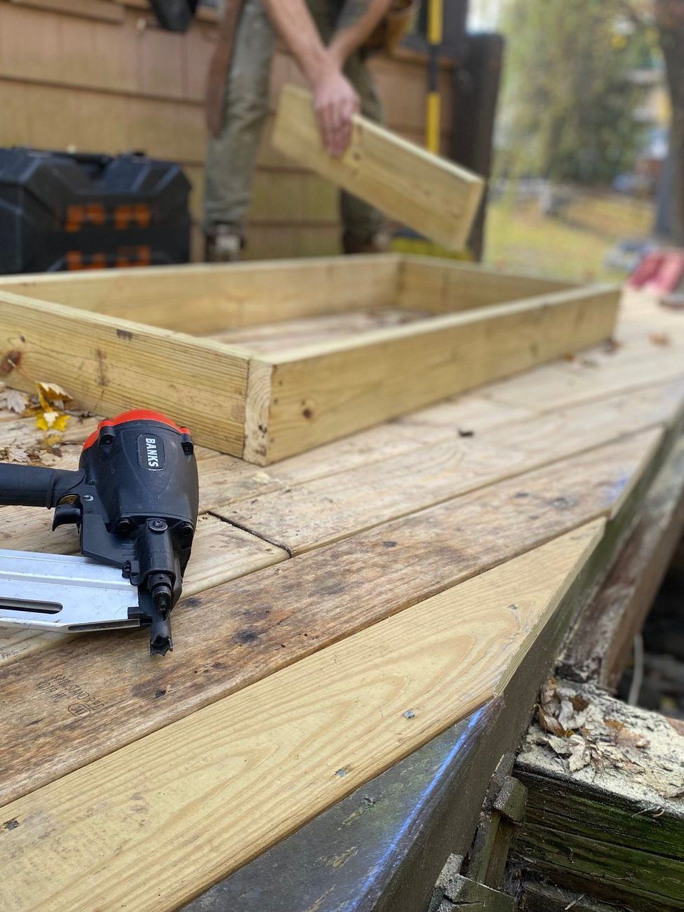 New joist framing and a nail gun on a deck build, old structure being replaced below