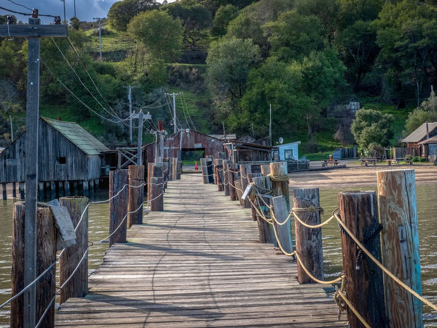 Rustic timber pier with rope handrails running out past a row of boat sheds