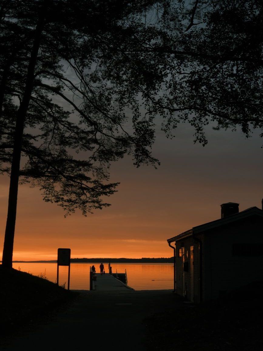 Dock and boat shed silhouetted against a burnt-orange sunset over still water