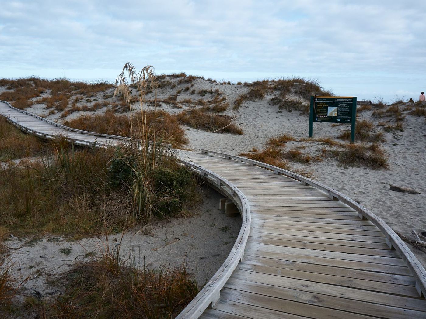 Wooden boardwalk winding over sand dunes and beach grass toward the shore