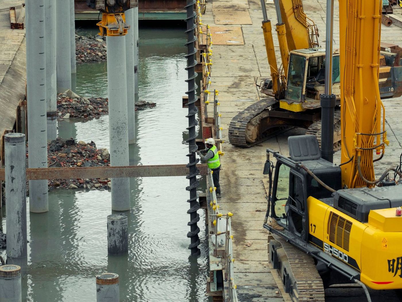 Excavator and crane setting steel sheet piles on a waterfront construction site