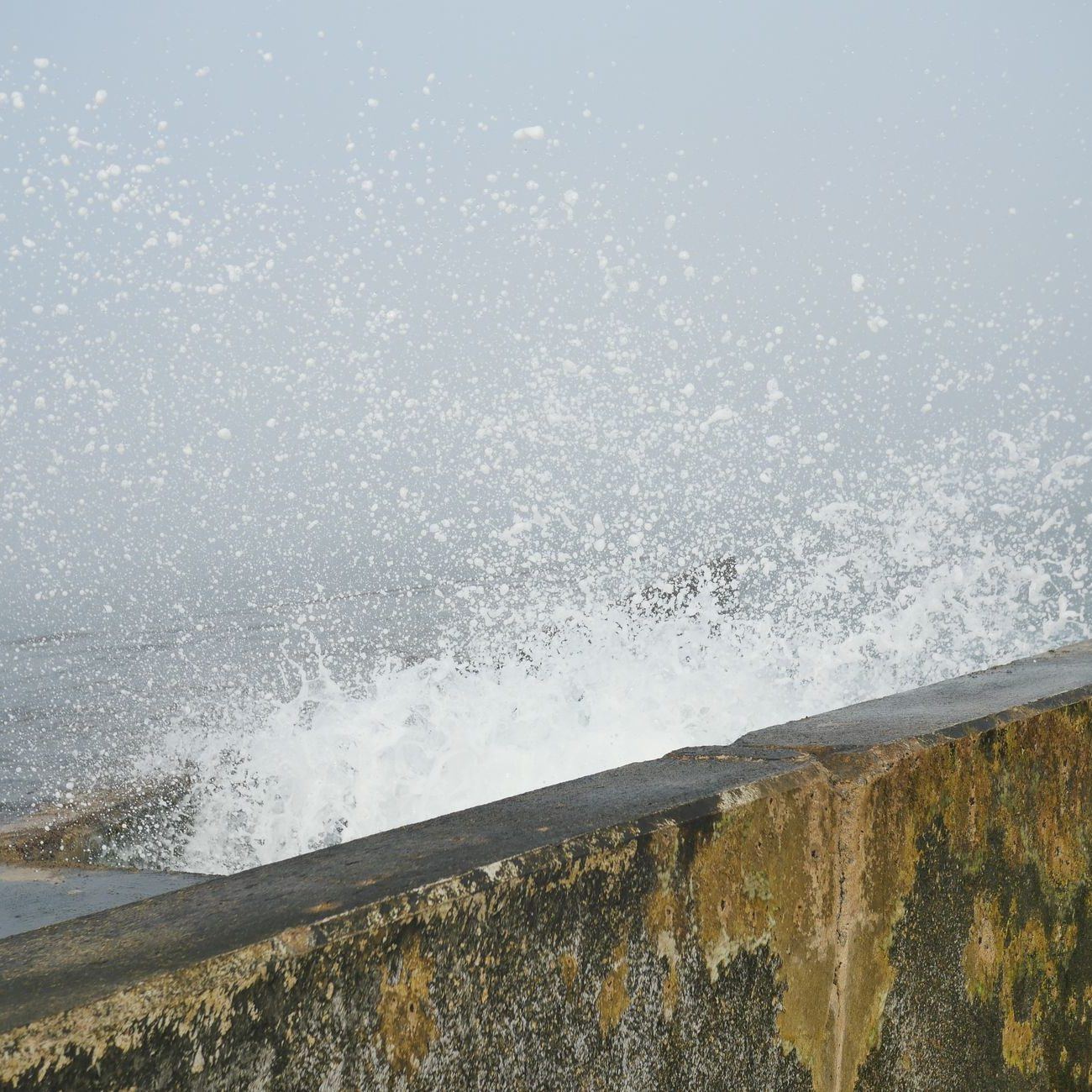 Wave breaking against the face of a concrete seawall, spray thrown over the crest