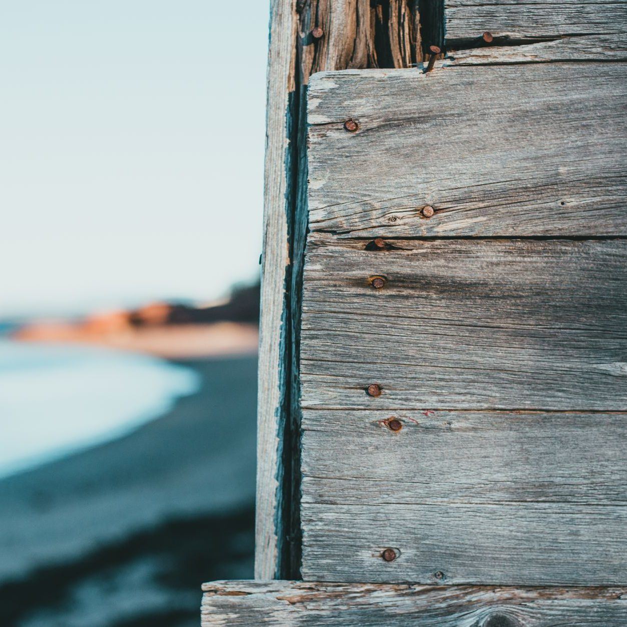 Close view of a timber seawall's planking with the beach and surf beyond it