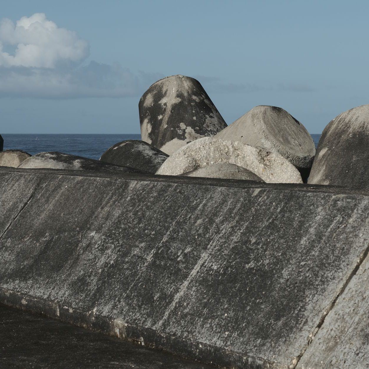 Concrete seawall with boulders piled along its top, open sea beyond