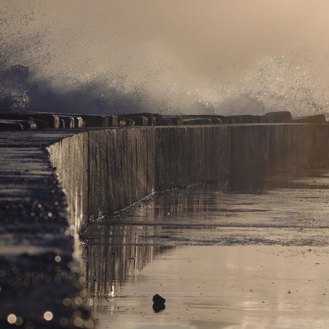 Curving concrete seawall along a beach with surf breaking against its base