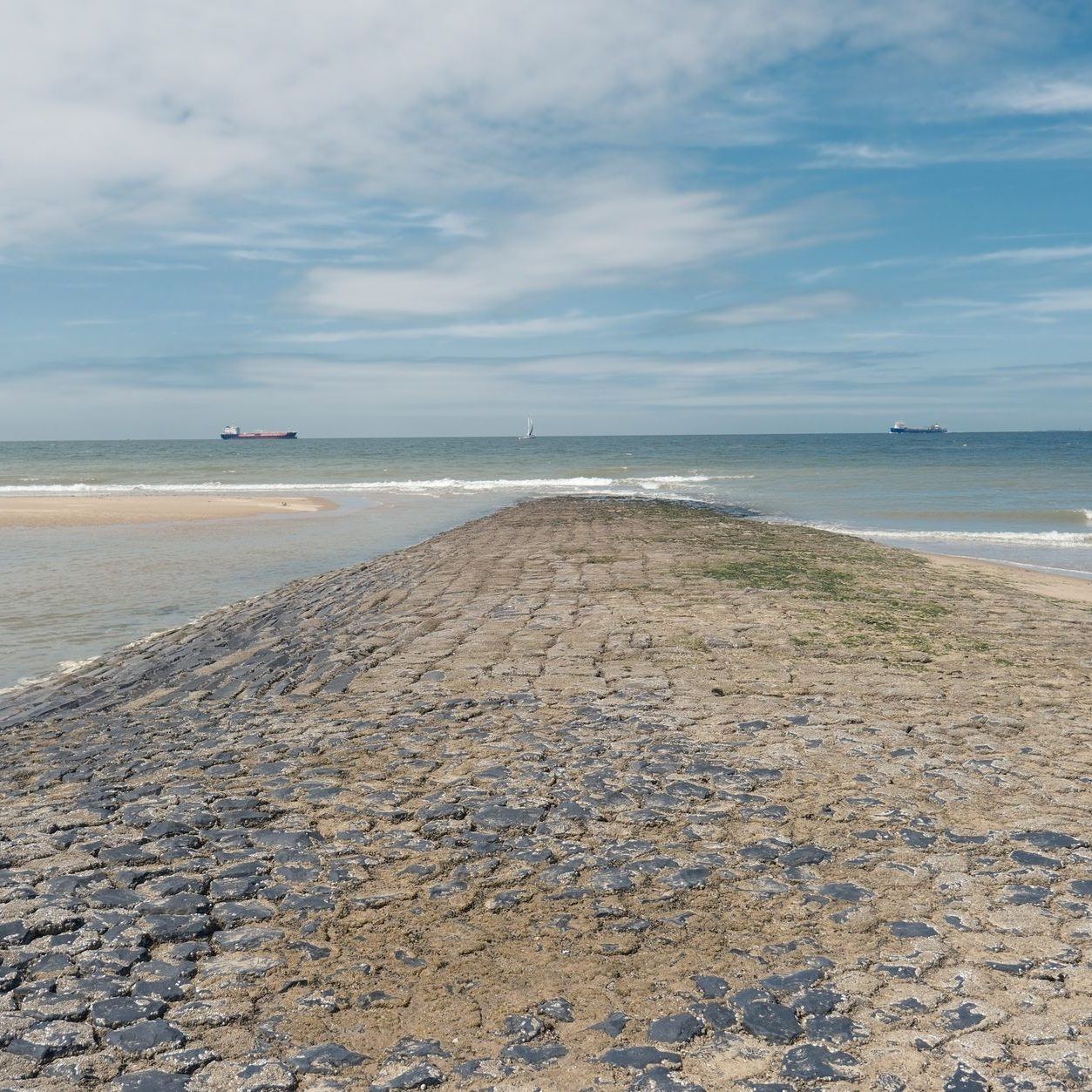 Stone-faced seawall running out along a sandy spit with the open sea on both sides