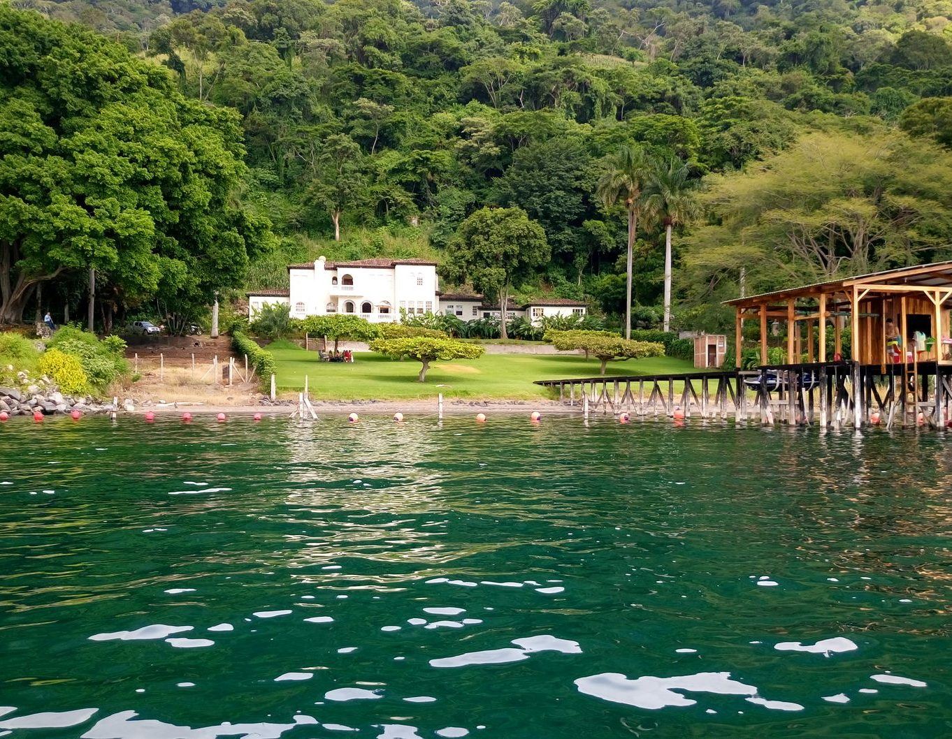 View from the water of a wooded shoreline with a covered dock and a home set back on the bank