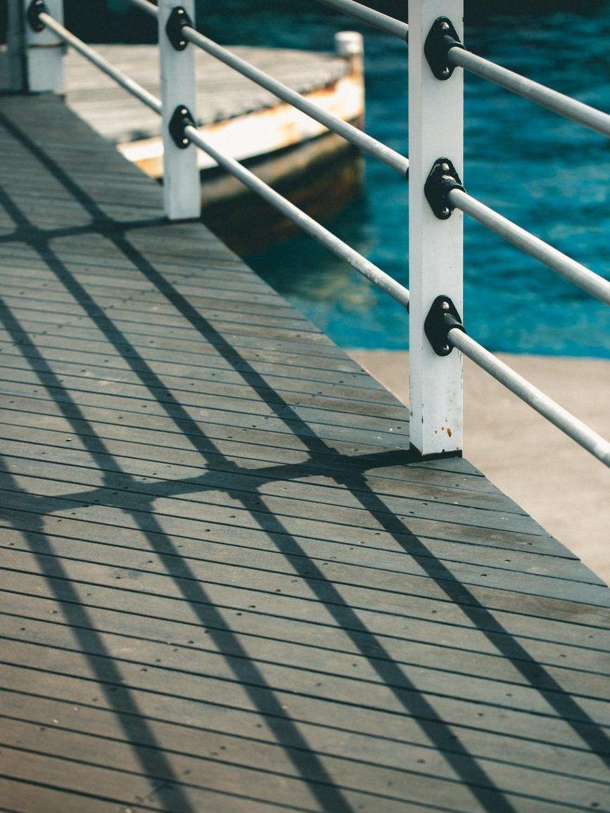 Timber dock rail with steel cable infill running out over bright blue water